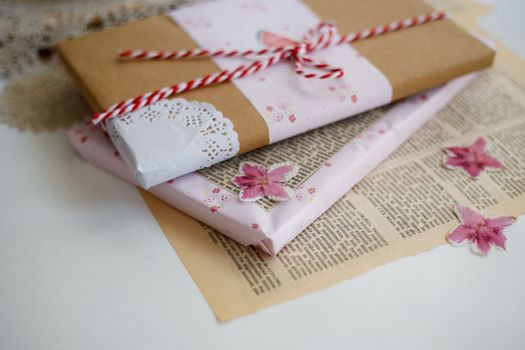 Emballages cadeaux élégants avec papier kraft, dentelle et fleurs séchées sur une surface claire.