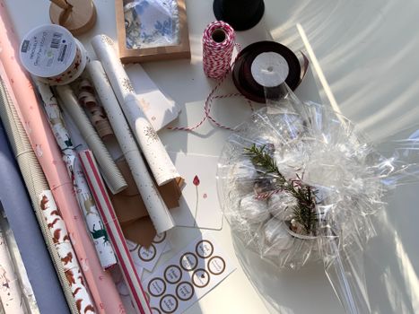 Matériaux d'emballage cadeaux, y compris du papier, des rubans et un panier décoré de plantes, sur une table lumineuse.